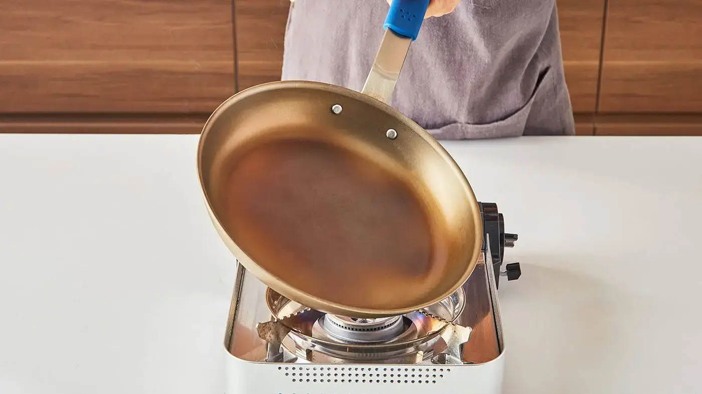 A person carefully seasoning a carbon steel pan.