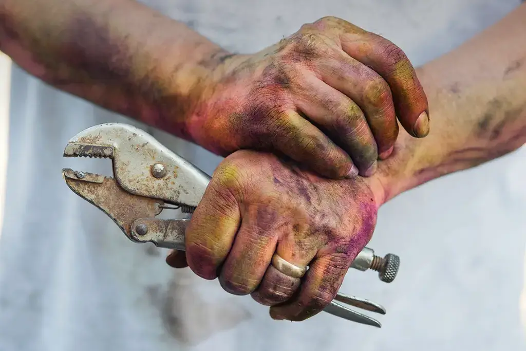 A craftsman's hand holding a rough prototype of a kitchen tool handle.
